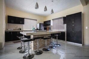Une cuisine moderne avec des meubles noirs, un plan de travail en marbre et trois tabourets de bar.