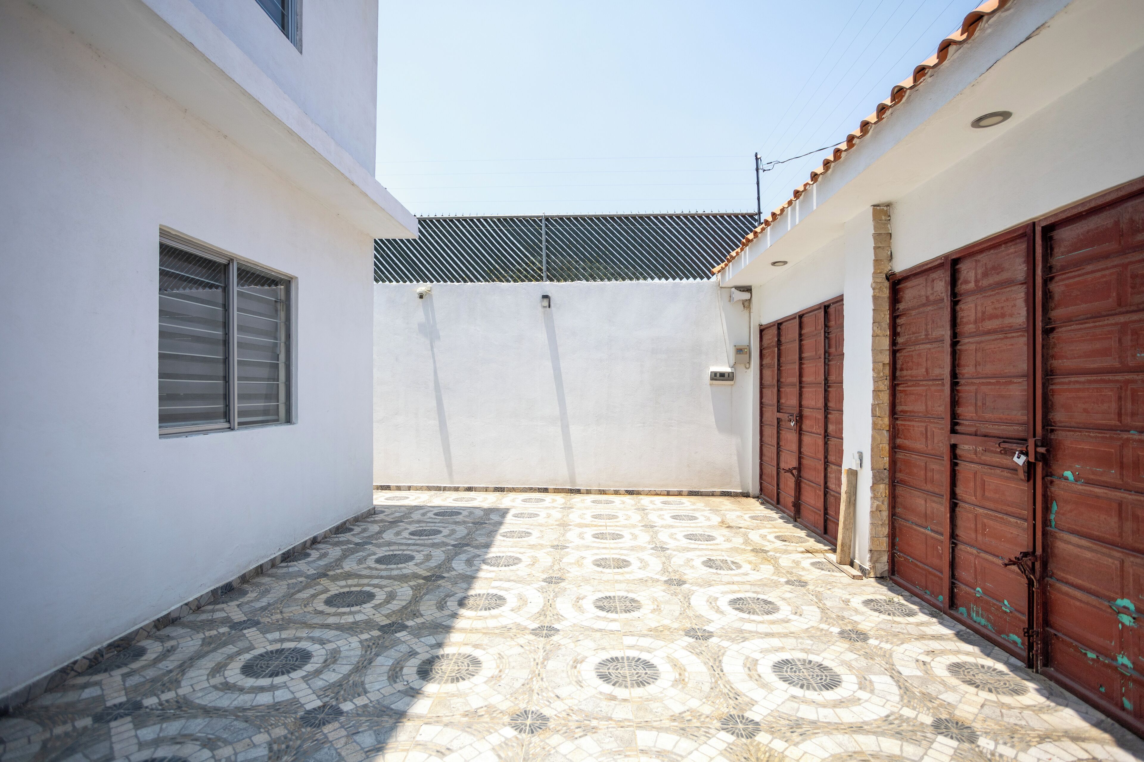 Un estrecho callejón con suelo de baldosas estampadas, una pared blanca y una cerca de metal.