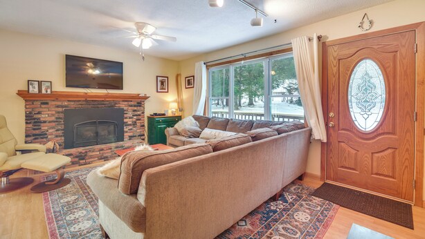 A living room with a fireplace, a sofa, a television, and a large window with curtains. - 1 Mi to Sugarbush Resort: Dog-Friendly Home! (Waitsfield)