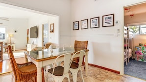 Un coin repas avec une table à plateau en verre, des chaises en osier et un mur blanc orné de tableaux.