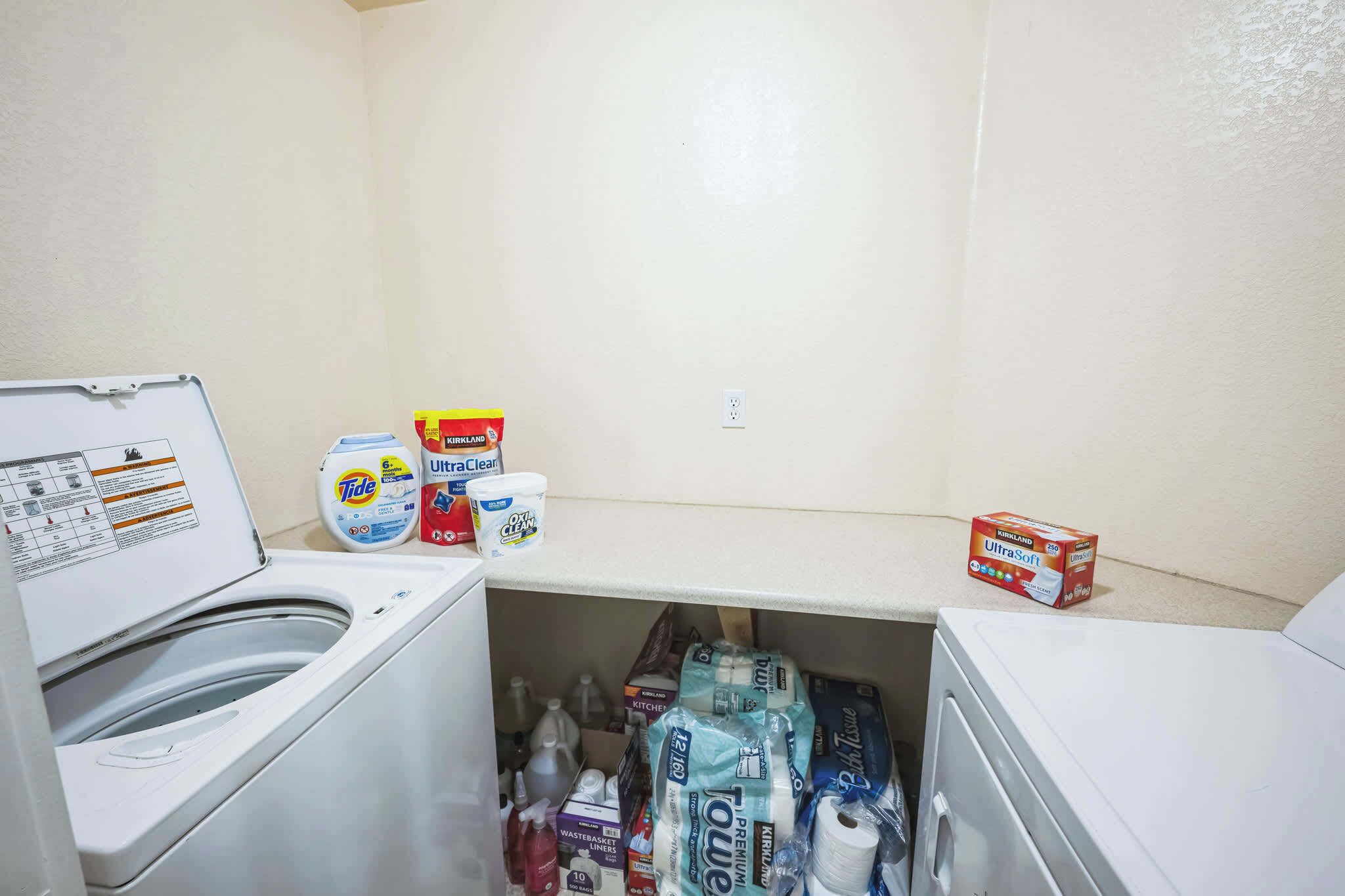 A laundry room with a washing machine, detergent, and fabric softener.