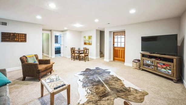A living room with a sofa, a coffee table, a TV on a wooden stand, a dining area with chairs and a table, and a door leading to another room. - Beautiful Backyard | Blocks from Old Town (Lafayette)
