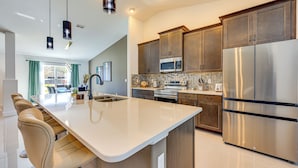 Een moderne keuken met een centraal eiland, roestvrijstalen apparatuur en een eethoek met een grote tafel en stoelen.