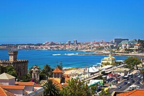 A coastal cityscape with a prominent historical tower, a beach, and a mix of modern and traditional architecture.