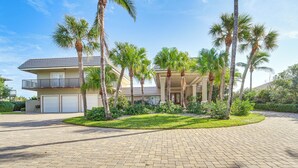 A residential property with a paved driveway, palm trees, and a two-story house with a balcony.