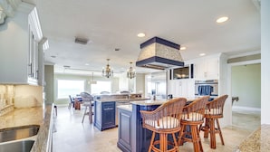 A spacious kitchen with a large island, dark cabinetry, and a chandelier.