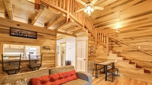 A wooden cabin interior with a sofa, a dining area, and a staircase. - Steps to Kentucky Lake: Cozy Cabin w/ Deck! (Waverly)
