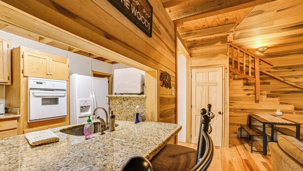 A kitchen with granite countertops, a built-in oven, and a sink. There is a wooden staircase leading to another level. - Steps to Kentucky Lake: Cozy Cabin w/ Deck! (Waverly)