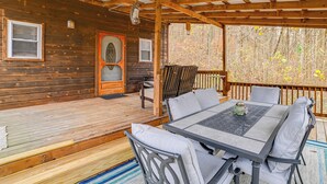 A covered wooden deck with a table and chairs, a wooden door, and a window with blinds. - Steps to Kentucky Lake: Cozy Cabin w/ Deck! (Waverly)
