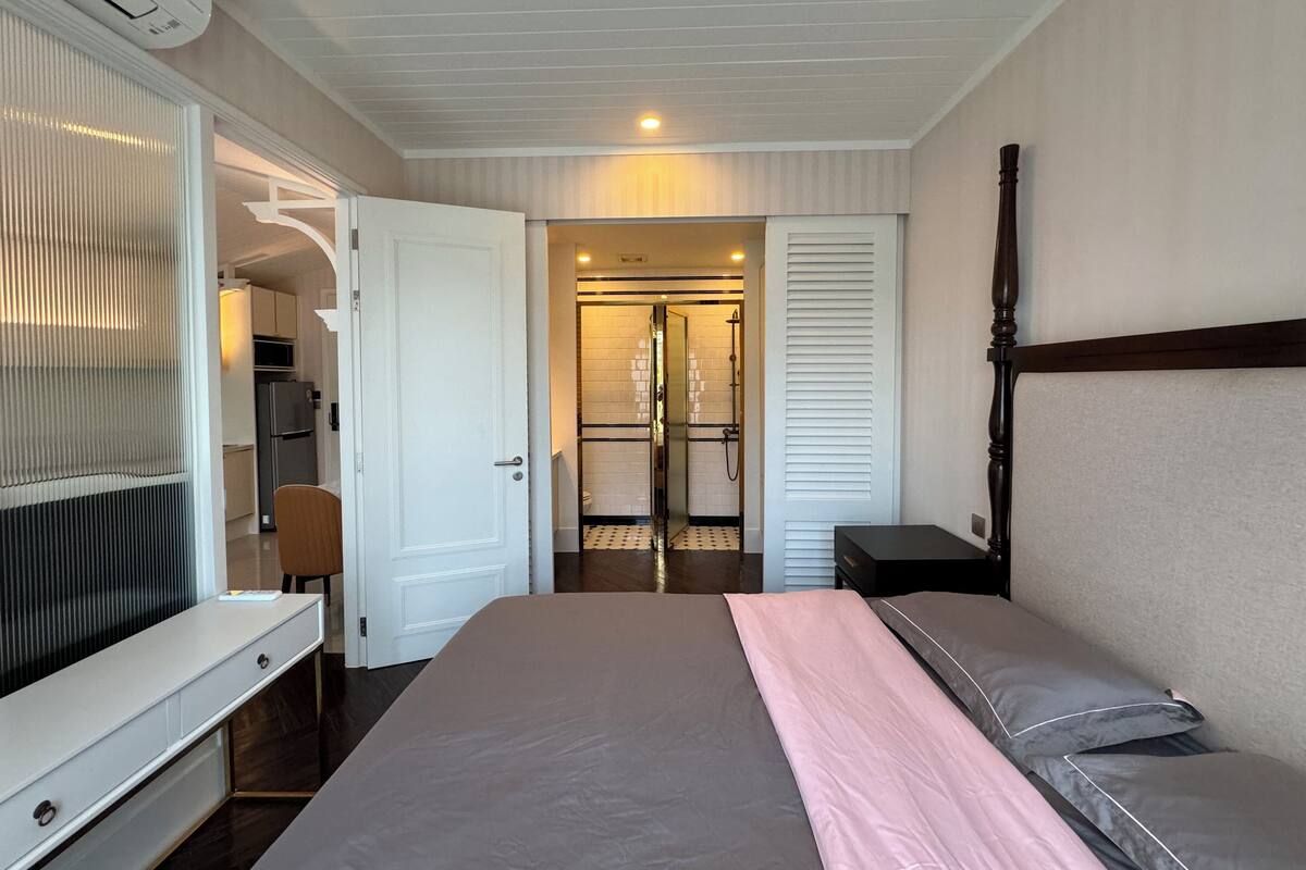 A hotel room with a bed, a desk, a wardrobe, and a bathroom visible through an open door.