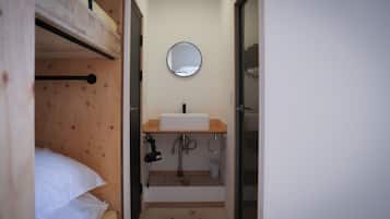 Una habitación pequeña y compacta con una cama individual superpuesta, un lavabo y un espejo.