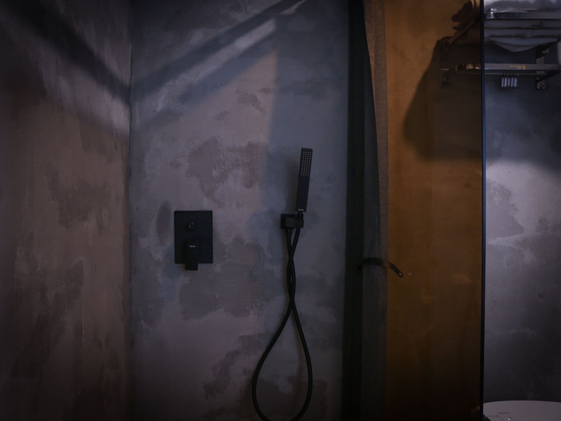 A shower area with a control panel and a handheld showerhead mounted on the wall.