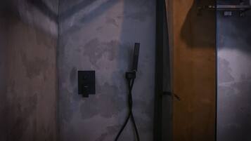 A shower area with a control panel and a handheld showerhead mounted on the wall.