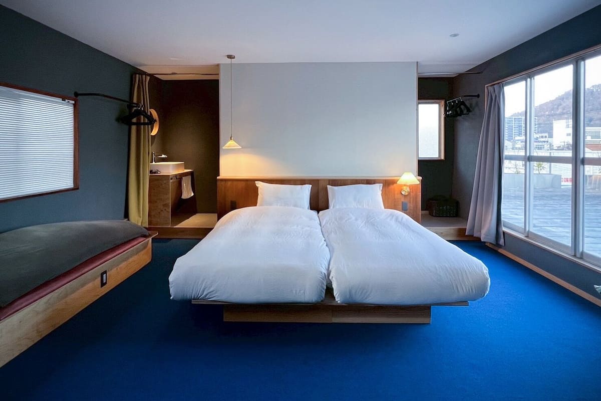 Ein Hotelzimmer mit einem großen Bett, einem Nachttisch, einer Lampe, einem Fenster und Blick nach draußen.