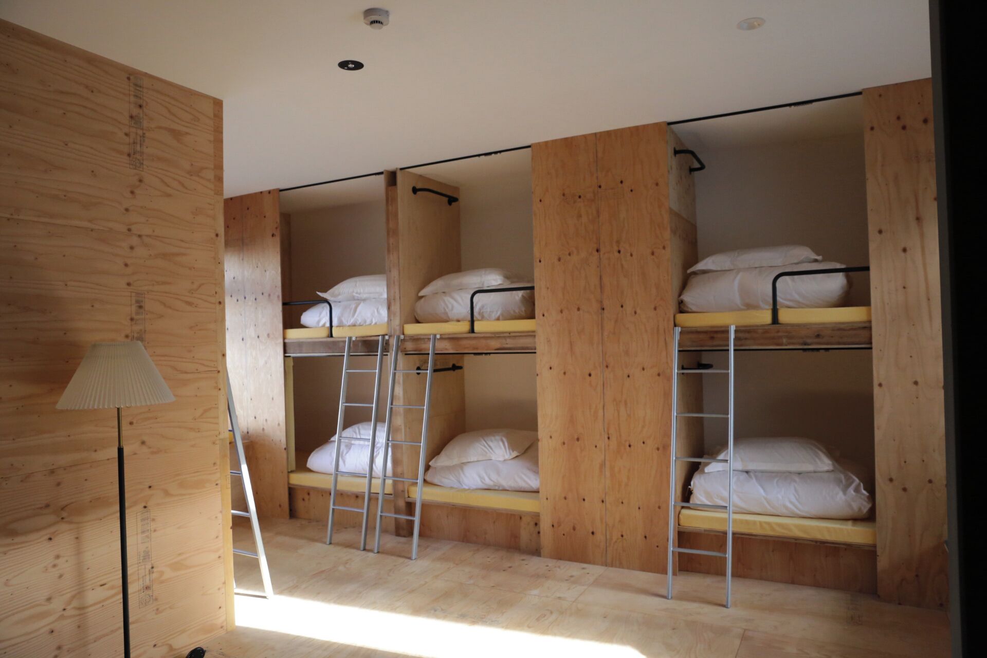 A dormitory room with bunk beds, wooden walls, a ladder, and a lamp.