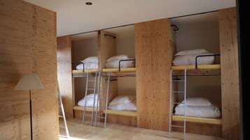 A dormitory room with bunk beds, wooden walls, a ladder, and a lamp.