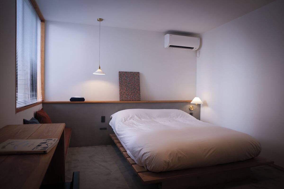 Ein kleines, modernes Schlafzimmer mit einem Einzelbett, einem Schreibtisch und einem Fenster mit Jalousien.