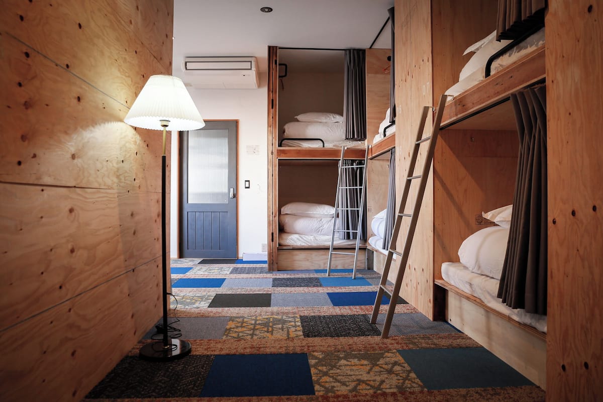 Ein Zimmer mit Etagenbetten, einer Stehleiter, einer Lampe und einem gemusterten Teppich.
