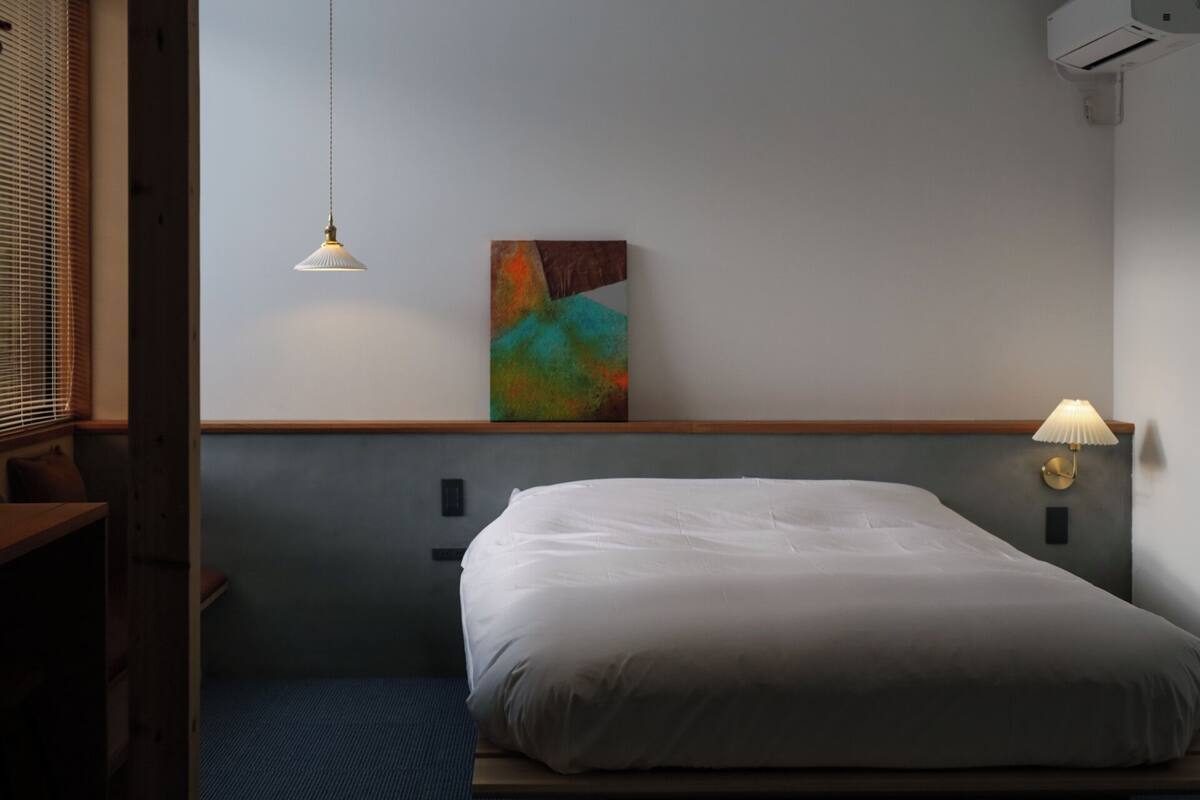 Ein Hotelzimmer mit Bett, Wandbild, Schreibtisch und Lampe.