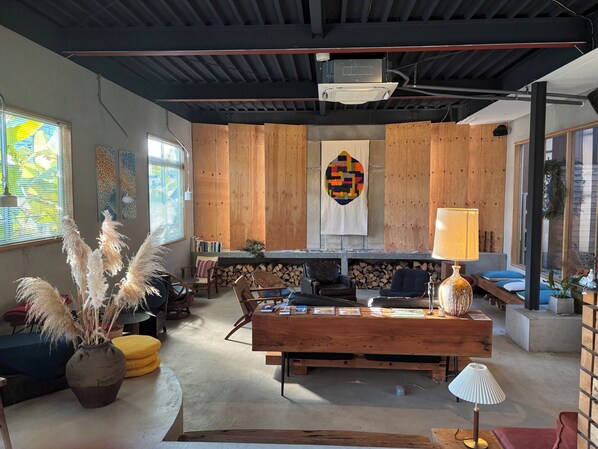 A cozy room with a wooden bench, a table with books, a hanging quilt, and a large window. - Lemonsea Onomichi (Onomichi)