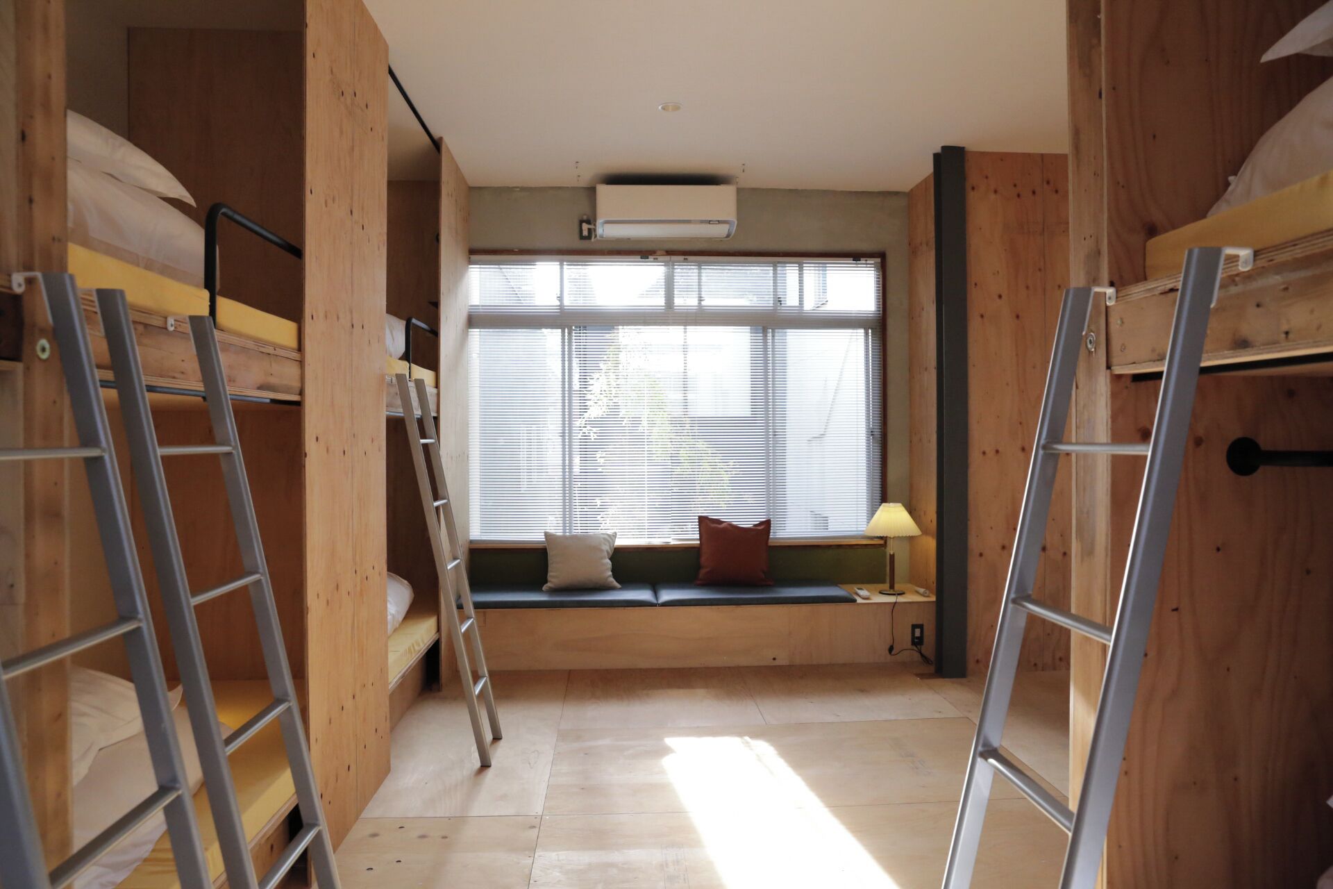 A room with bunk beds, a window with blinds, a ladder, and a wall-mounted air conditioner.