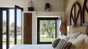 A bedroom with a large window, a bed with striped pillows, a wooden wardrobe, and a decorative mirror.