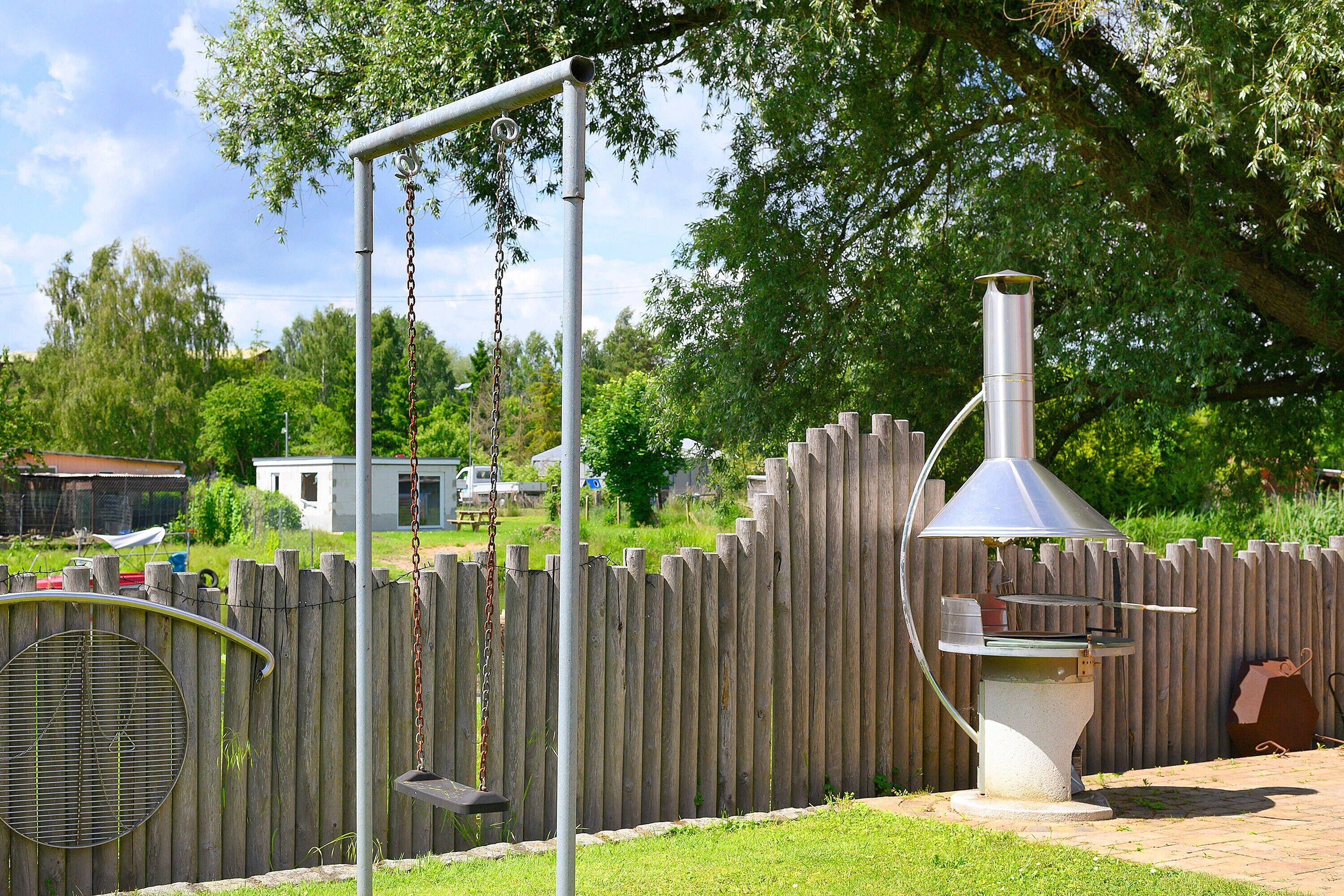 A backyard with a swing set, a grill, and a wooden fence.