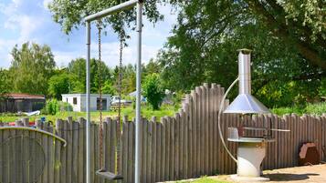 A backyard with a swing set, a grill, and a wooden fence.