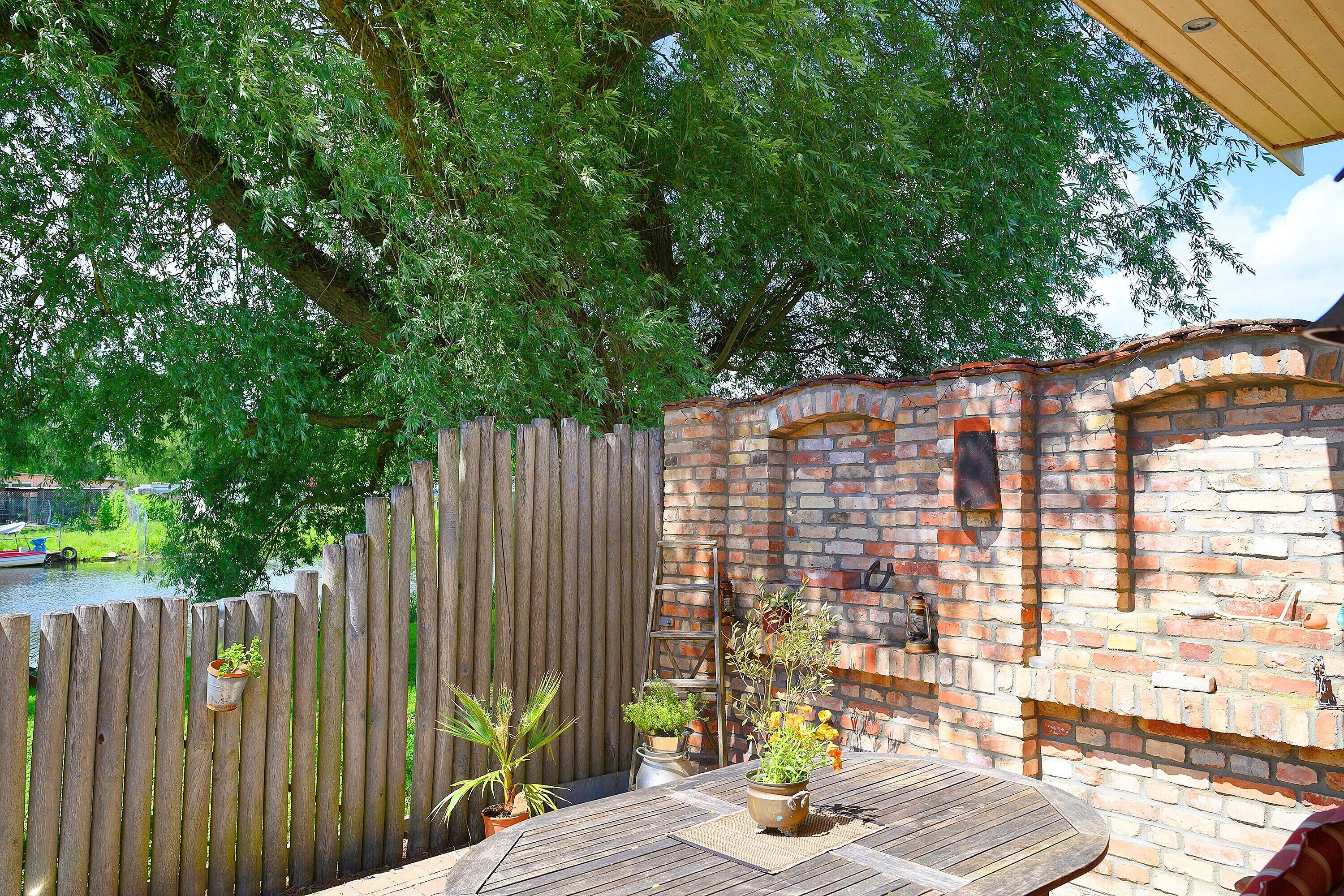 A wooden deck with a brick wall, potted plants, and a ladder leaning against the wall.