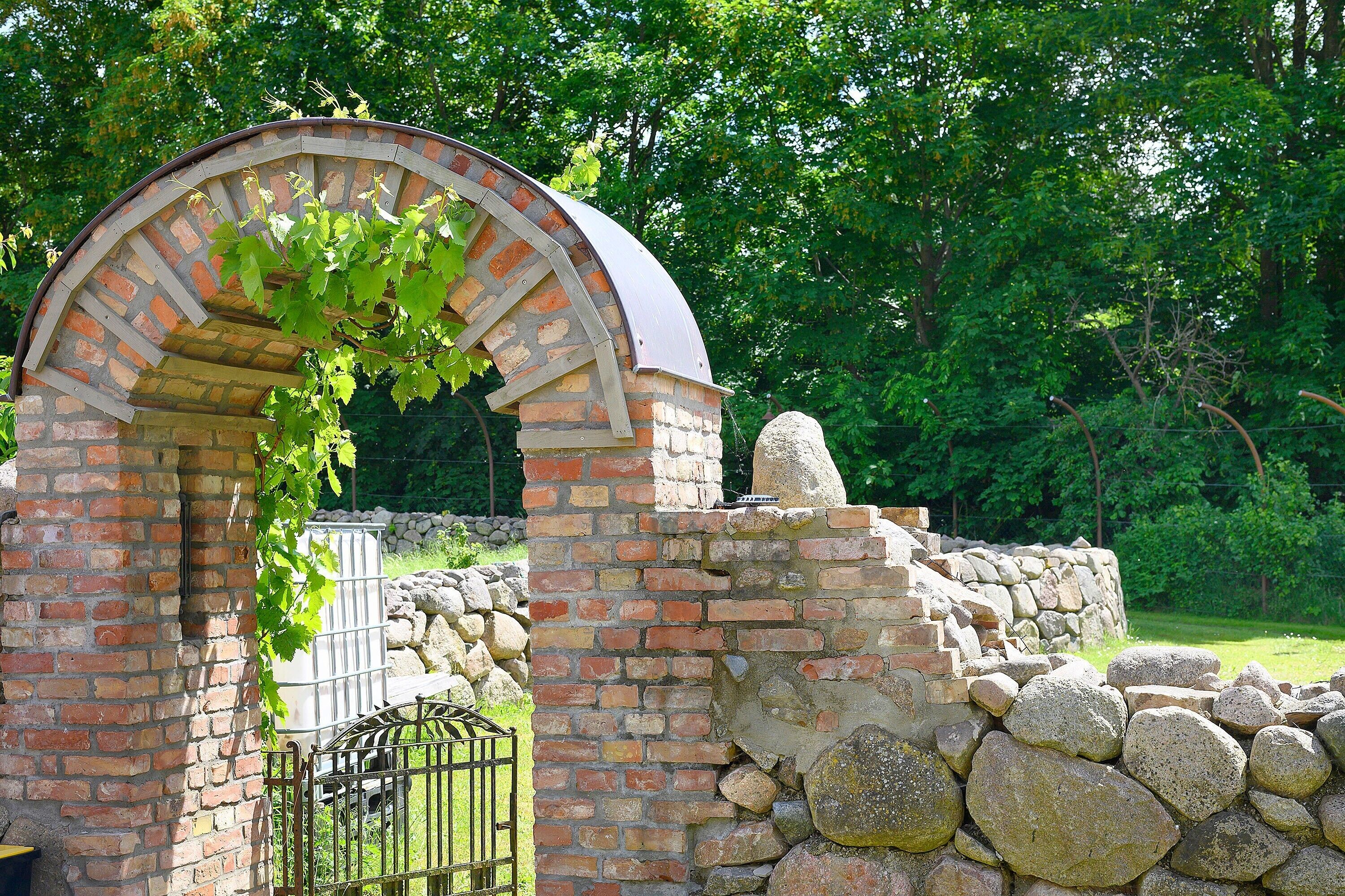 A brick structure with a curved archway, a stone wall, and a metal gate.