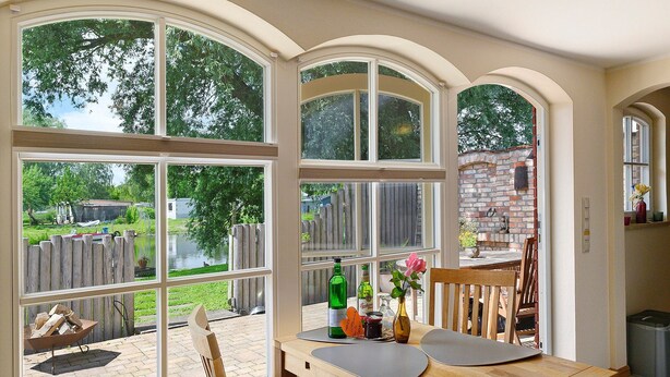 A dining area with a view of a backyard, a brick wall, and a wooden fence. - Holiday Home 'Reiseoase' with Lake View, Wi-Fi and Air Conditioning (Bützow)