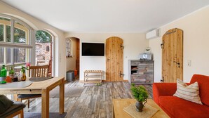 A room with a wooden dining table, a red sofa, a TV mounted on the wall, and a wooden cabinet. - Holiday Home 'Reiseoase' with Lake View, Wi-Fi and Air Conditioning (Bützow)