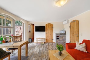 Una habitación con una mesa de comedor de madera, un sofá rojo, un televisor montado en la pared y un armario de madera.