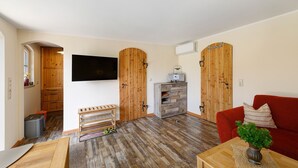 A living room with a red sofa, wooden cabinets, a TV, and a wooden door. - Holiday Home 'Reiseoase' with Lake View, Wi-Fi and Air Conditioning (Bützow)