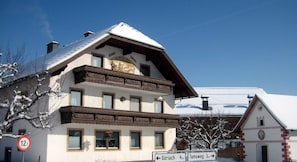A traditional Alpine-style building with a sloped roof, multiple windows, and a sign indicating nearby locations.
