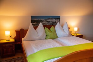 Ein Hotelzimmer mit einem Bett, zwei Nachttischen, einer Lampe und einem Gemälde einer Berglandschaft.