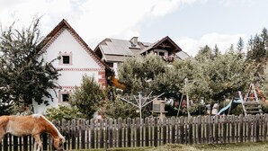 Una casa tradicional con cerca de madera, un caballo pastando al frente y un parque infantil al fondo.