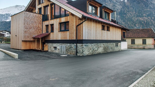 Una casa di legno con tetto spiovente, ampie finestre e fondamenta in pietra.