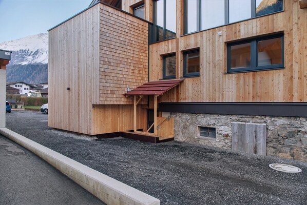A modern wooden building with a stone wall, a small window, and a gravel driveway.