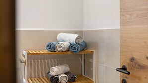 Un bagno con ripiano in legno con asciugamani arrotolati e porta in vetro.