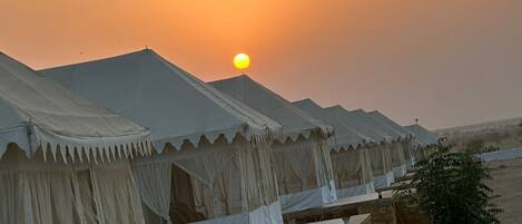 A row of tents with a stone foundation, set against a sunset backdrop.