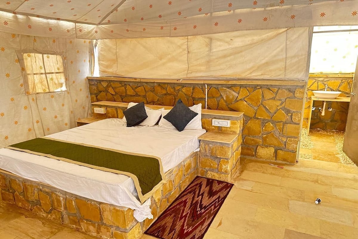 A bedroom with a stone wall bed, a stone bench, a small sink, and a window with a view.