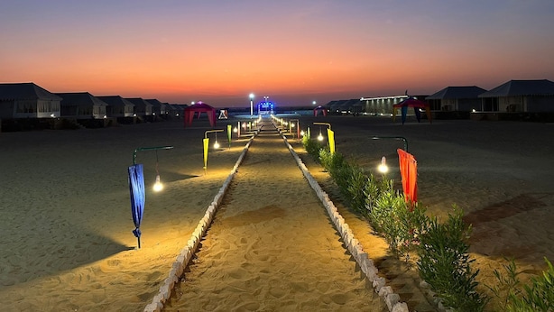 A pathway leading to beach huts with a sunset in the background. - Raghav Resort Jaisalmer (Jaisalmer)