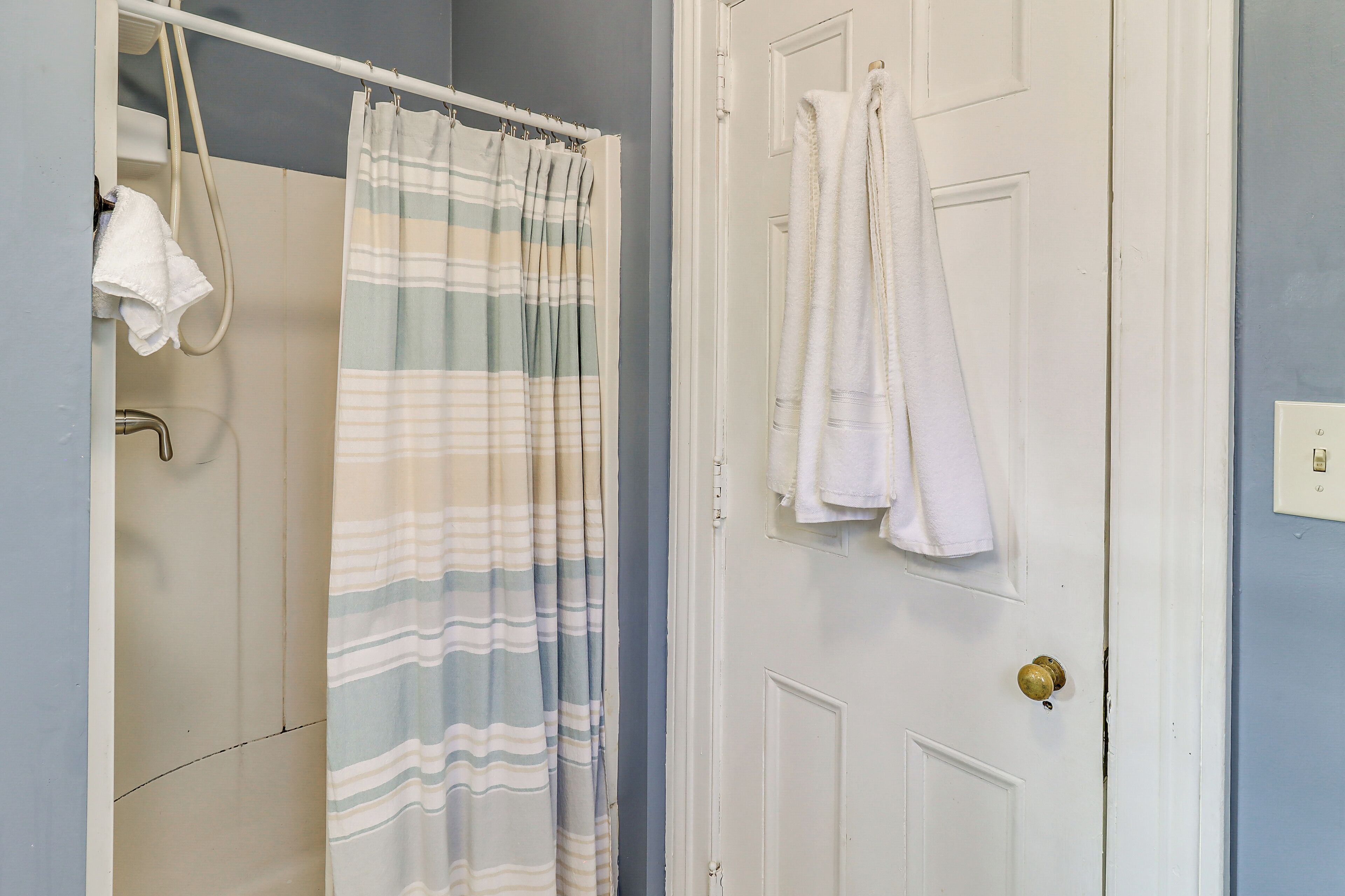 A bathroom with a shower curtain, a towel rack, and a door with a towel hanging on it.