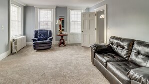 A living room with a leather sofa, a blue armchair, and a small table with a lamp. - 1 Block to Downtown Adrian: Spacious Home! (Adrian)
