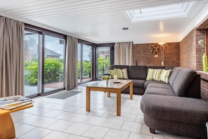 Ein modernes Wohnzimmer mit einer Couch, einem Couchtisch und Blick auf Grün hinter großen Schiebetüren.