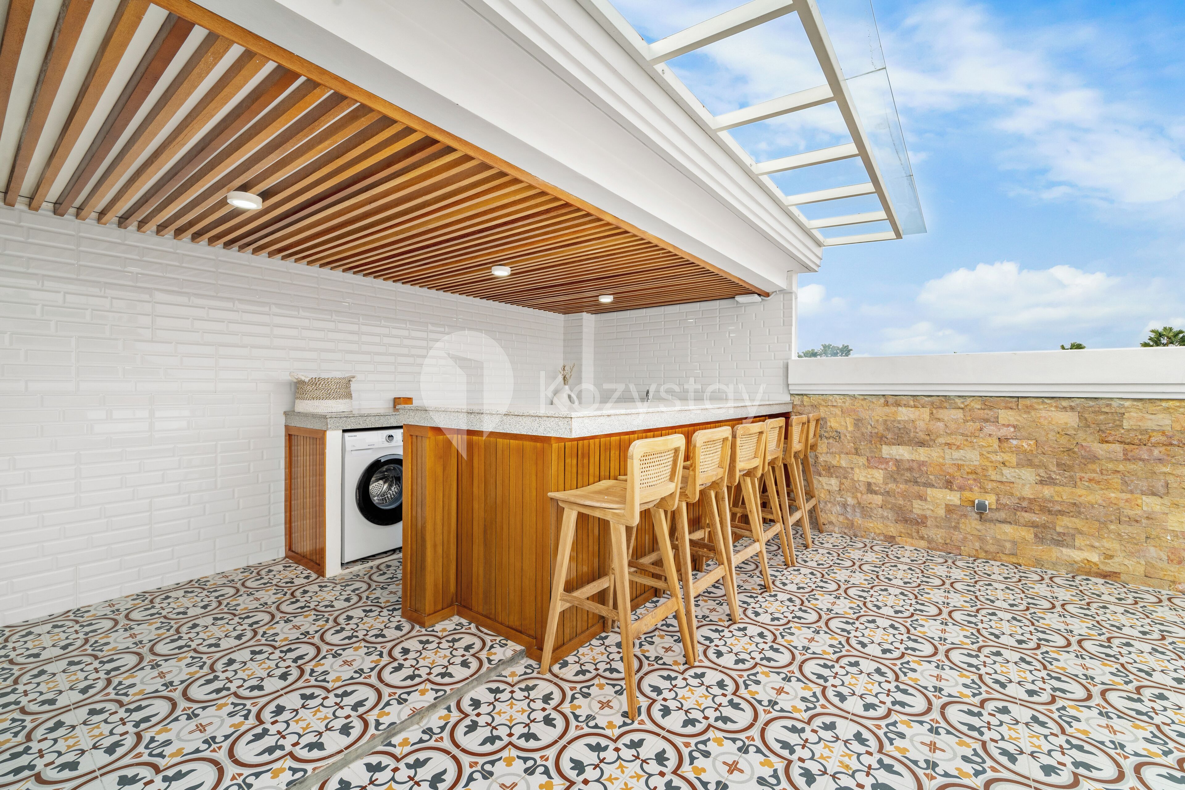 A kitchen with a wooden ceiling, a washing machine, and a bar area with stools.
