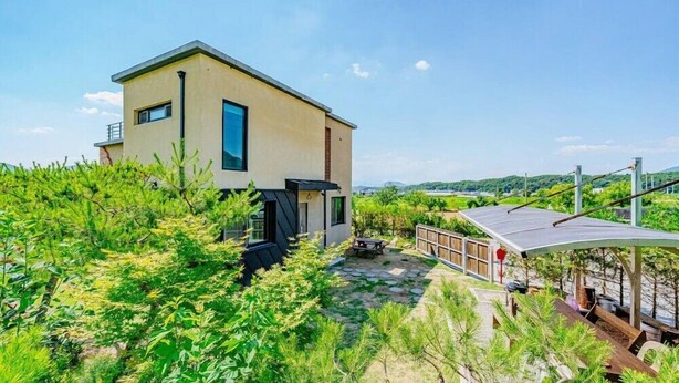 A modern two-story house with a patio area, surrounded by lush greenery and a clear view of the landscape. - Chuncheon Stay 266 (Chuncheon)