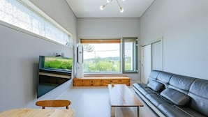 A modern living room with a large window, a black leather sofa, a wooden bench, and a television. - Chuncheon Stay 266 (Chuncheon)
