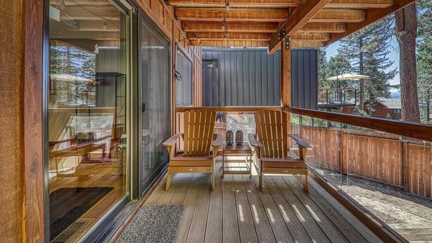 A wooden deck with two Adirondack chairs and a table, overlooking a forested area. - 4 BR Retreat with Lakeview and Hot Tub (Kings Beach)